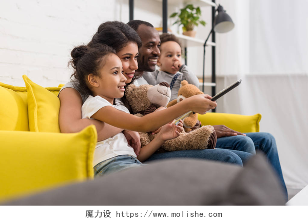 幸福的一家人在沙发上看电视美丽的年轻家庭一起看电视在沙发上